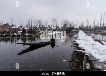 Srinagar, India. 4 febbraio 2024. Un uomo fila la sua barca sul lago dal durante le nevicate. Le pianure del Kashmir stanno assistendo a una moderata nevicata, mentre nei tratti più alti della valle sono state segnalate forti nevicate. La valle del Kashmir ha subito una nevicata fresca che ha sconvolto la normale vita delle persone. Le operazioni di volo, il trasporto di superficie e le attività di routine della vita si arrestarono. (Immagine di credito: © Idrees Abbas/SOPA Images via ZUMA Press Wire) SOLO USO EDITORIALE! Non per USO commerciale! Foto Stock