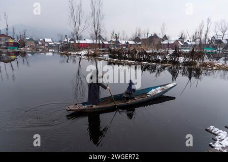 Srinagar, India. 4 febbraio 2024. Una donna rema la sua barca sul lago dal durante le nevicate. Le pianure del Kashmir stanno assistendo a una moderata nevicata, mentre nei tratti più alti della valle sono state segnalate forti nevicate. La valle del Kashmir ha subito una nevicata fresca che ha sconvolto la normale vita delle persone. Le operazioni di volo, il trasporto di superficie e le attività di routine della vita si arrestarono. (Immagine di credito: © Idrees Abbas/SOPA Images via ZUMA Press Wire) SOLO USO EDITORIALE! Non per USO commerciale! Foto Stock