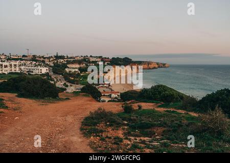 Pittoresco tramonto sulle scogliere e sull'oceano, con la silhouette di una città che aggiunge un tocco di fascino urbano al paesaggio naturale mozzafiato di Lagos Foto Stock