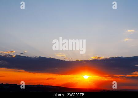 Le vivaci sfumature del tramonto dipingevano il cielo con nuvole e raggi di sole, un caldo bagliore sulla silhouette della città Foto Stock