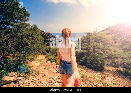 Seguitemi. La ragazza tiene e conduce il suo fidanzato per mano tra le montagne in riva al mare nel viaggio estivo. Insieme riposano in un giorno di sole Foto Stock