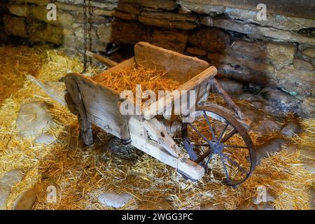 vecchia carriola in legno con ruota in metallo nel fienile con paglia Foto Stock