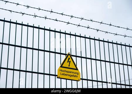 Warnschild für Hochspannung an einem Zaun 04.02.2024, Limburgo: Symbolfoto, Illustrationsbild, Symbolbild, Illustrationsfoto Ein gelbes Warnschild mit der Aufschrift Hochspannung Lebensgefahr ist deutlich sichtbar an einem Zaun mit Stacheldraht befestigt. Der Hintergrund zeigt einen grauen, bewölkten Himmel, era Die ernste Warnung noch hervorhebt. Die visuelle Kombination aus dem Warnschild, dem Stacheldrahtzaun und dem düsteren Himmel vermittelt ein starkes Gefühl von Vorsicht und Gefahr. Limburg Hessen Germania *** cartello di avvertimento per alta tensione su una recinzione 04 02 2024, foto simbolo Limburgo, illu Foto Stock