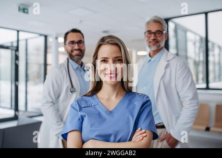 Ritratto di una dottoressa in piedi di fronte a colleghi di sesso maschile. Bella infermiera in uniforme in una moderna clinica privata, che guarda la macchina fotografica. Foto Stock