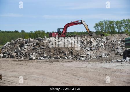 Una discarica di detriti con un escavatore che pulisce il disordine. Foto Stock
