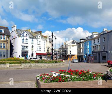 Vista dei negozi di Fore Street nel centro della città con graziose aiuole in primo piano, Seaton, Devon, Regno Unito, Europa. Foto Stock