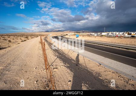 Un'autostrada nel deserto con un'ombra sul lato della strada. L'ombra proviene da un albero solitario, ed è l'unica cosa che spezza la monotonia del de Foto Stock