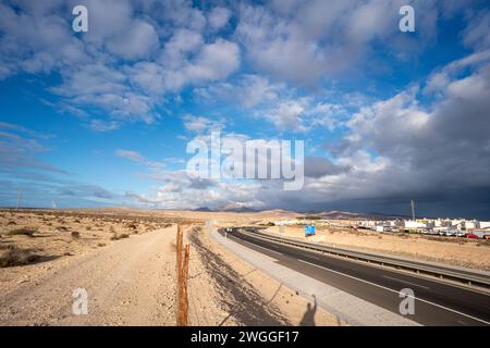 Un'autostrada nel deserto con un'ombra sul lato della strada. L'ombra proviene da un albero solitario, ed è l'unica cosa che spezza la monotonia del de Foto Stock