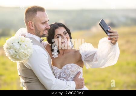 Una giovane coppia di nozze si sta facendo un selfie mentre si gode un momento romantico nel parco. Foto Stock