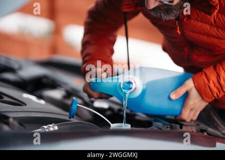 Versare il liquido lavavetri invernale nel serbatoio dell'auto durante l'inverno, proteggendolo dal congelamento. Foto Stock