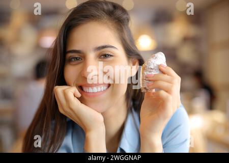 Donna felice sorridente che tiene uno spuntino e guarda la macchina fotografica all'interno di un bar Foto Stock