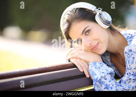 Una donna rilassata ti guarda mentre ascolti l'audio con le cuffie in un parco Foto Stock