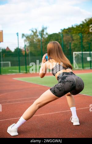 Foto di giovane donna sportiva accentrata in abbigliamento sportivo all'aperto in uno stadio che fa affondamento in esercizio Foto Stock