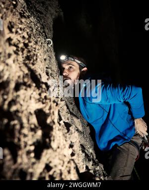 Un arrampicatore si concentra mentre tenta di agganciarsi a un bullone durante una salita notturna nel Massachusetts occidentale. Foto Stock