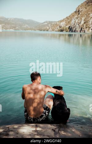 Ragazzo che abbraccia il suo cane in un lago con montagne sullo sfondo Foto Stock