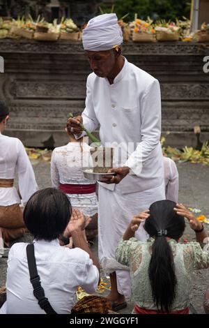 Sacerdote che versa acqua Santa su due donne durante il rituale indù Foto Stock