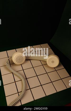 Ricevitore telefonico vintage su piastrelle bianche e sfondo verde Foto Stock
