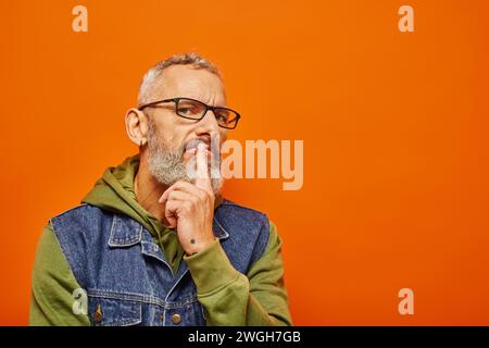 bell'uomo maturo con cappuccio verde e barba grigia in posa su sfondo arancione Foto Stock