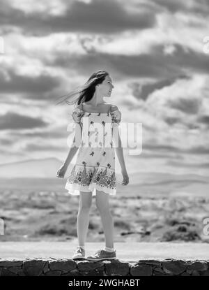 fotografia in bianco e nero di una ragazza adolescente con un abito estivo bianco su uno sfondo di nuvole Foto Stock