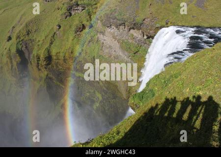 Bordo di una cascata con due arcobaleni e ombre di fotografi a Skógafoss in Islanda Foto Stock