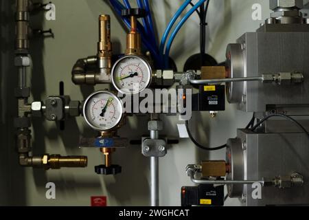Parte di apparecchiature automatizzate con due misuratori meccanici, cavi e tubi metallici installati all'interno di un grande impianto industriale o di una fabbrica Foto Stock