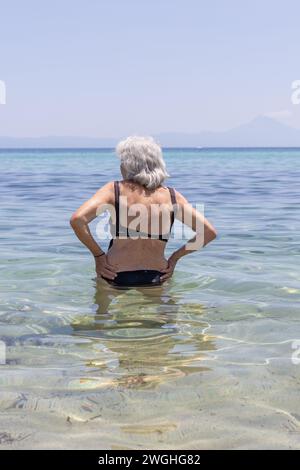 donna anziana in costume da bagno che entra in mare Foto Stock