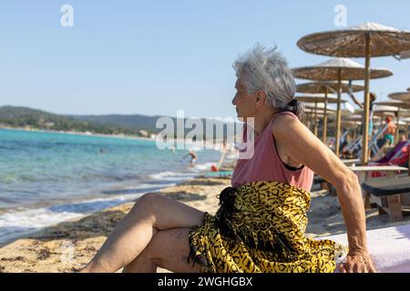 signora anziana seduta sulla spiaggia che si gode la sua vacanza Foto Stock