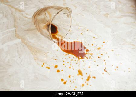 Fuoriuscita di caffè da una tazza di vetro trasparente su fondo in marmo, messa a fuoco morbida in primo piano Foto Stock