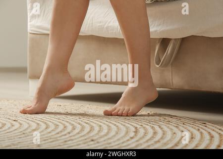 I piedi di una donna a piedi nudi sul pavimento accanto al letto la mattina nella sua casa o in hotel Foto Stock