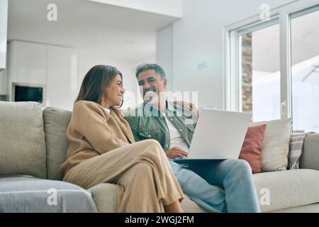 Coppia matura felice che usa un computer portatile che si rilassa sul divano nel soggiorno. Colpo sincero. Foto Stock