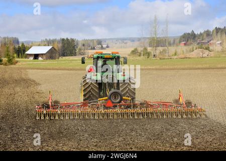 Agricoltore che lavora nel campo con il trattore John Deere e il coltivatore Potila Magnum 800 Plus per seminativi in primavera, vista posteriore. Salo, Finlandia. 14 maggio 2022. Foto Stock