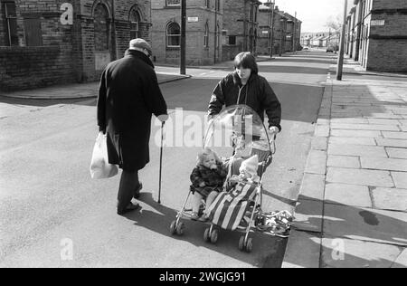 Madre che spinge la carrozza in strada 1989s UK. Il marciapiede acciottolato fa tremare la carrozza, un vecchio che cammina in strada per sicurezza, ha paura di cadere su un marciapiede irregolare. Niente auto, niente linee gialle. Shipley, Bradford West Yorkshire Inghilterra 1981. Saltaire era un villaggio vittoriano costruito intorno al Salts Mill, che prende il nome da Sir Titus Salt. Fu chiusa nel 1986 dopo 133 anni come fabbrica tessile. Oggi HOMER SYKES, patrimonio dell'umanità dell'UNESCO Foto Stock