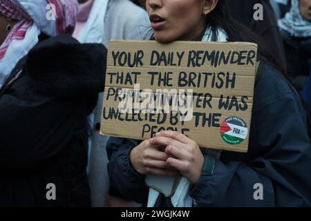 Una donna ha un cartello che dice che il primo Ministro britannico non è stato eletto mentre centinaia di migliaia di persone hanno marciato sulla marcia nazionale per la Palestina chiedendo un cessate il fuoco. Foto Stock