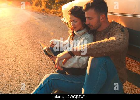 Bella coppia in viaggio, si sta prendendo una pausa dalla guida e sta cercando indicazioni sul tablet. Foto Stock