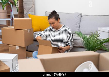 La donna toglie oggetti fuori scatola per il design vicino al divano in casa Foto Stock