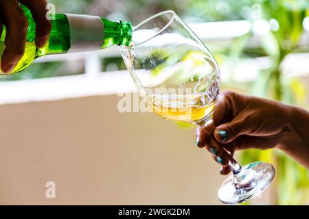 Mano di un uomo che versa birra dalla bottiglia al bicchiere tenuto da una donna. Foto Stock