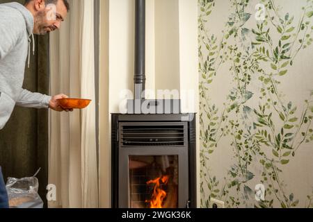 Uomo che riempie una stufa a pellet. Piano cottura collocato nel soggiorno della casa. Concetto di riscaldamento domestico sostenibile per il futuro. Foto Stock