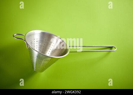 Primo piano di un collander da cucina in metallo su un tavolo verde utilizzato per la produzione delle puree. Foto Stock