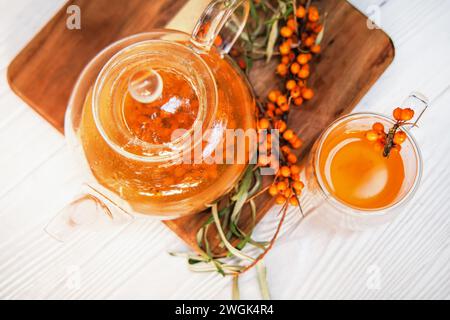 Vivaci bacche di spinoso marino che si infondono in una teiera trasparente per un'estrazione gustosa. rimedio omeopatico per la vitalità Foto Stock