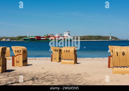 Strandkörbe an der Kieler Förde bei herrlichem Frühjahrswetter im Hintergrund passiert ein Frachtschiff den Leuchtturm Foto Stock