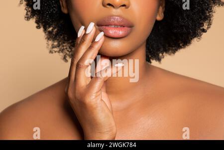 Primo piano delle labbra e del mento di una donna nera, toccando il viso, sfondo beige Foto Stock