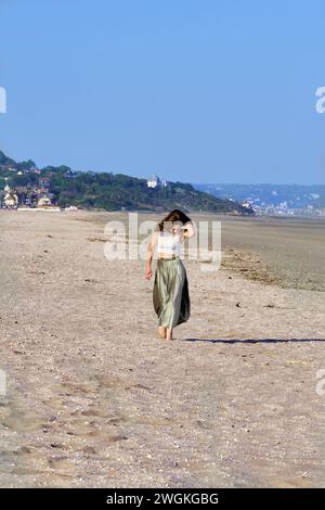 Giovane donna che cammina da sola su una spiaggia sabbiosa in una soleggiata giornata estiva, sulla costa francese Foto Stock