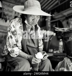 Vecchia signora che prepara fiori in vendita in un tempio buddista in Thailandia Foto Stock