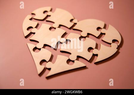 Primo piano di alcuni pezzi separati di un puzzle che insieme formano un cuore su un bianco rustico superficie in legno raffigurante l'idea di rottura o cooperatio Foto Stock