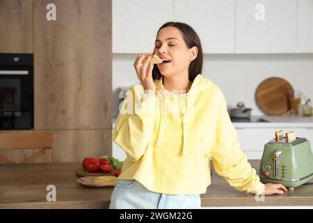 Giovane bella donna che mangia un gustoso toast con burro di arachidi in cucina Foto Stock