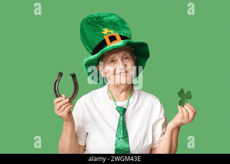 Donna anziana in cappello da leprechaun con ferro di cavallo e trifoglio su sfondo verde. St Festa di Patrick Foto Stock