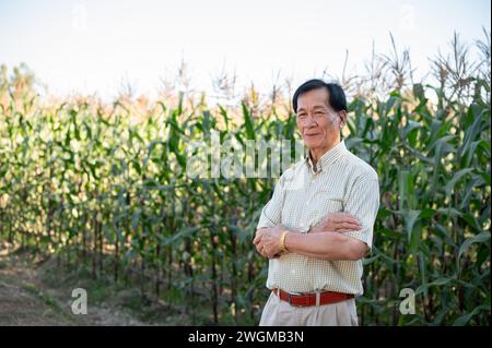 Un grande agricoltore asiatico di successo è orgoglioso con le braccia incrociate nel suo campo di grano. Concetto agricolo Foto Stock