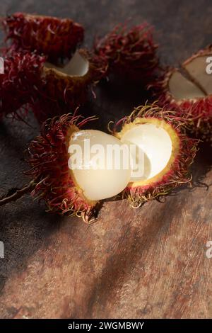 rambutan maturo, frutta tropicale sbucciata originaria del sud-est asiatico su uno sfondo rustico in legno, messa a fuoco selettiva con illuminazione e spazio spettacolari Foto Stock