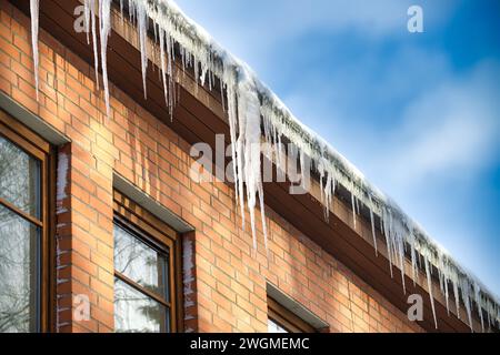 Ghiaccioli cristallini e luccicanti che si sono formati a causa delle condizioni climatiche gelide, appesi al bordo di una residenza in legno marrone Foto Stock