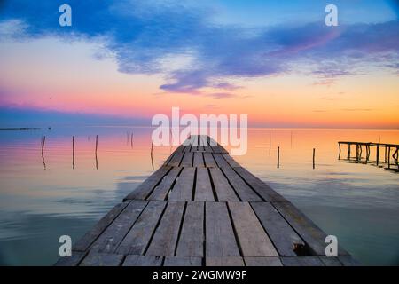 Una vista panoramica di un molo di legno su un lago al tramonto Foto Stock